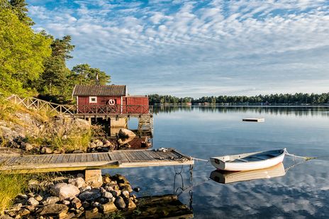 Ein See mit einer skandinavischen Hütte und einem Steeg in Schweden