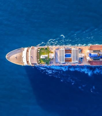 Luftaufnahme eines Kreuzfahrtschiffs auf dem tiefblauen Meer mit sichtbarer Heckwelle