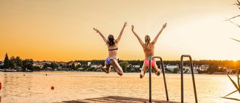 Zwei Frauen  die bei Sonnenuntergang in einen Badesee springen