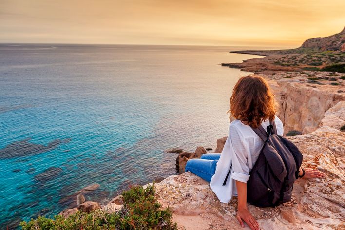 Frau sitzt auf einer Klippe in Zypern mit Blick auf das Meer