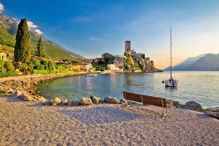 Strand in Malcesine am Gardasee mit Blick auf die Scaligerburg und Segelboot bei Sonnenuntergang