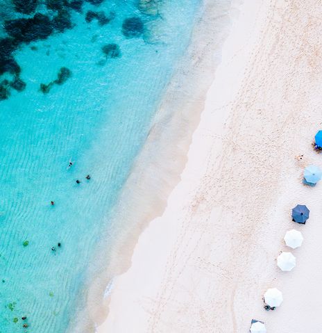 Luftaufnahme eines weißen Sandstrands auf Bali mit bunten Sonnenschirmen und türkisblauem Meer
