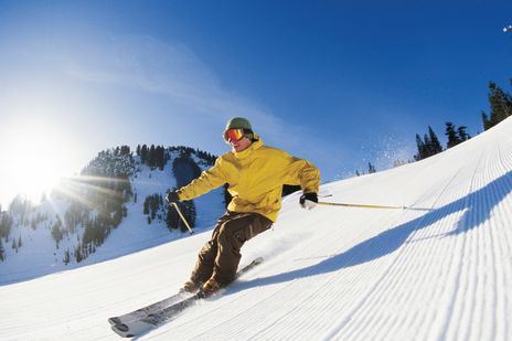 Skifahrer carvt schwungvoll eine Piste bei blauem Himmel hinunter
