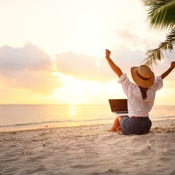 Frau sitzt im Sand und hat einen Laptop auf dem Schoß