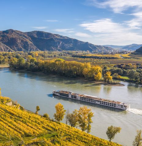 Flusskreuzfahrtschiff fährt entlang der Donau in Österreich mit Weinbergen am Ufer
