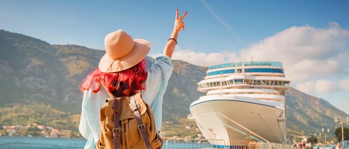Eine Frau mit pinken Haaren winkt einem Kreuzfahrtschiff am Anleger zu