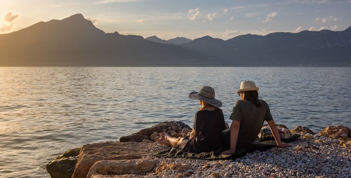 Paar sitzt am Ufer des Gardasees und genießt den Sonnenuntergang mit Blick auf die Berge