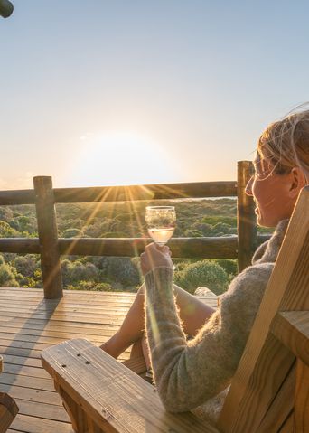 Frau sieht auf einer Terrasse und genießt den Sonnenuntergang mit einem Glas Wein