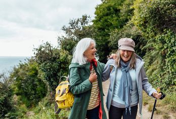 Zwei Freundinnen wandern lachend mit Rucksäcken auf sonnigem Waldweg