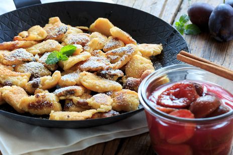 Österreichische Mehlspeise mit Puderzucker und fruchtigem Beerenkompott wird in einer Pfanne serviert.