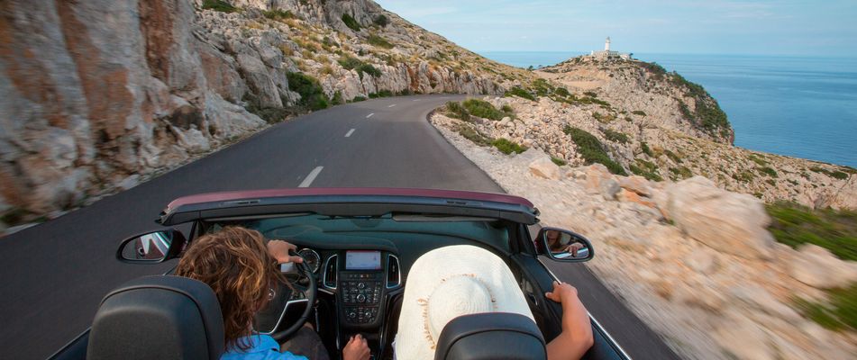 Personen fahren im Cabrio am Cap de Formentor eine Küstenstraße entlang, Blick aufs Meer