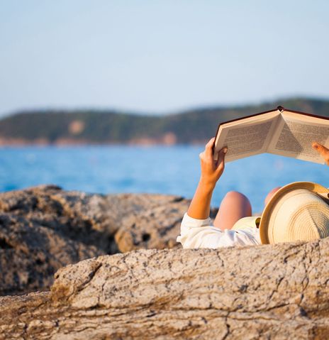 Frau auf Felsen am Meer mit Buch