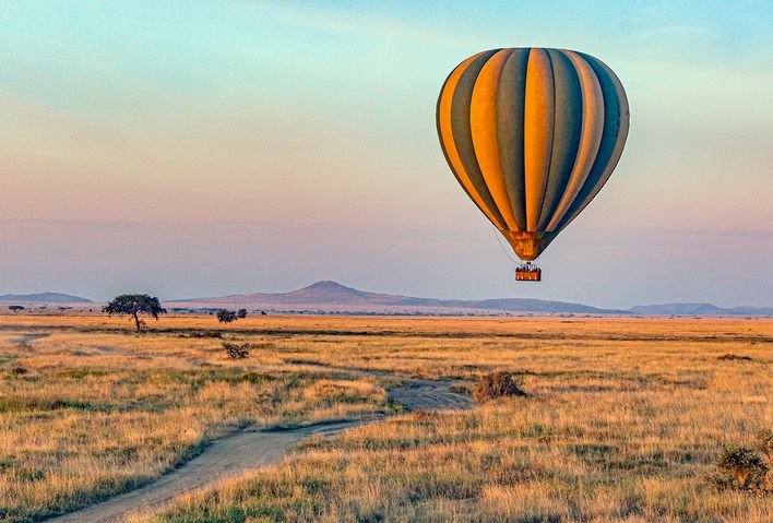 Heißluftballon fliegt bei Sonnenaufgang über den Serengeti Nationalpark in Tansania