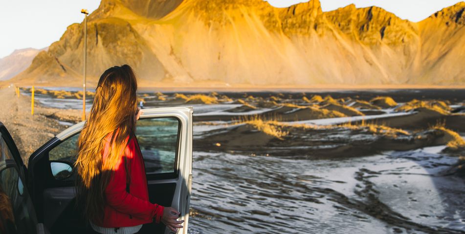 Frau in Rückansicht, die in Island aus einem Auto aussteigt und die Landschaft betrachtet