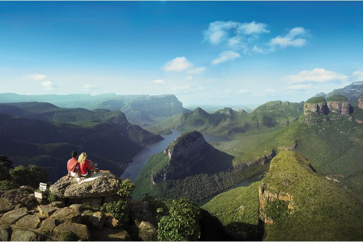 Zwei Wanderer sitzen auf einem Felsen mit weitem Blick über die grünen Schluchten Mpumalangas