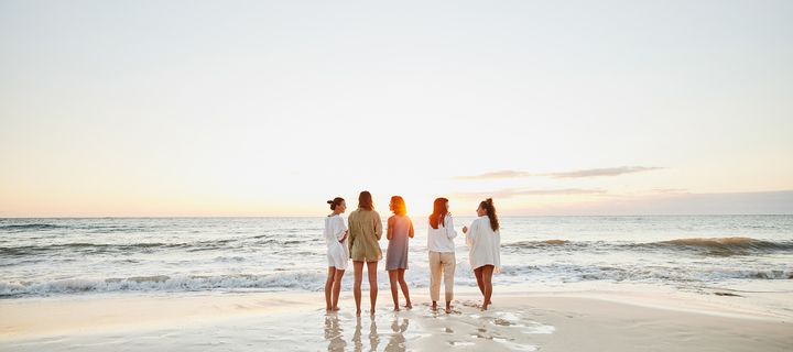 Gruppe von Frauen steht gemeinsam am Meer und blickt auf den Sonnenuntergang