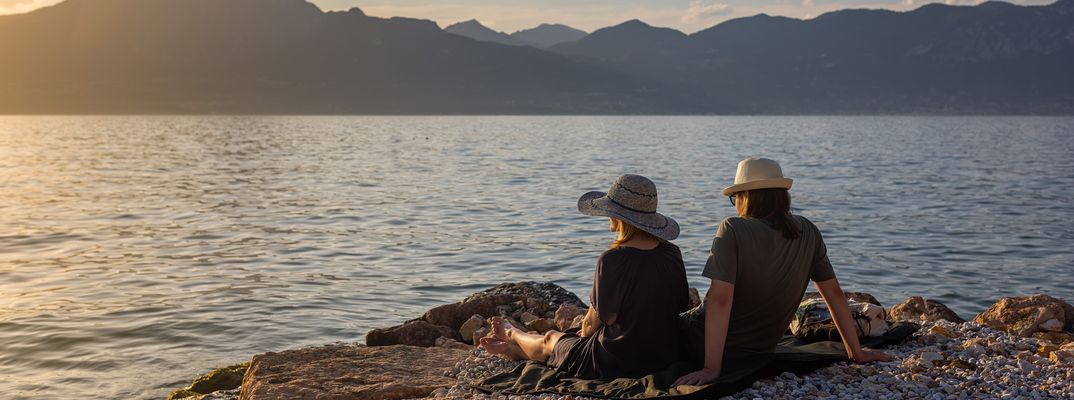 Paar sitzt am Ufer des Gardasees und genießt den Sonnenuntergang mit Blick auf die Berge