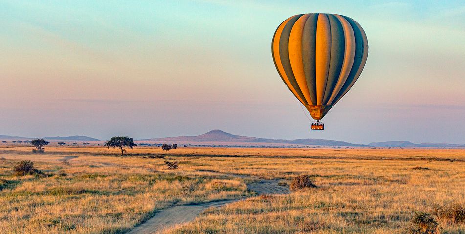 Heißluftballon fliegt bei Sonnenaufgang über den Serengeti Nationalpark in Tansania