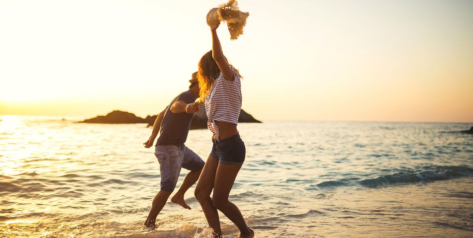 Fröhlich tanzendes Paar am Meer bei Sonnenuntergang