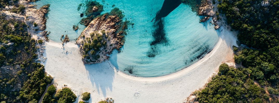 Luftaufnahme von einem Strand auf Sardinien mit weißem Sand und türkisfarbenem Wasser