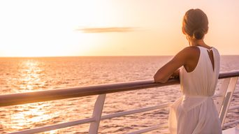 Frau an einer Schiffsreling und blickt in den Sonnenuntergang