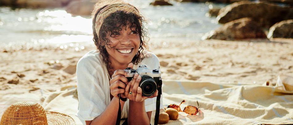 Frau liegt auf einer Decke am Strand mit Kamera und macht Fotos im Sand