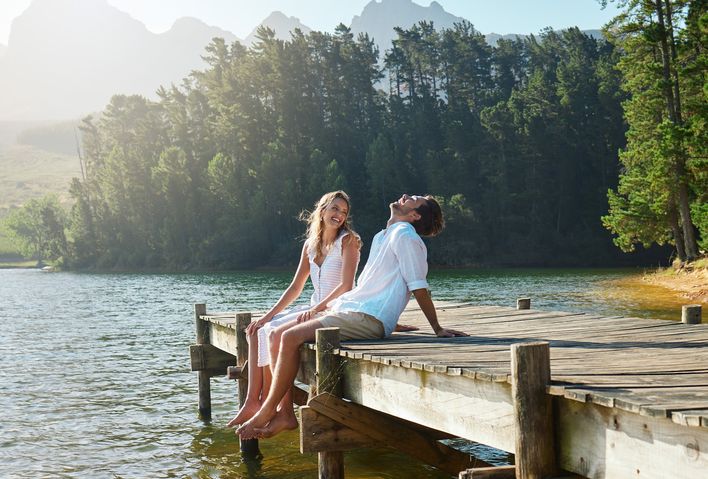 Paar sitzt im Sommer auf einem Steg am See und lacht vor Freude