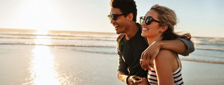 Glückliches Paar mit Sonnenbrillen bei einem Spaziergang am Strand