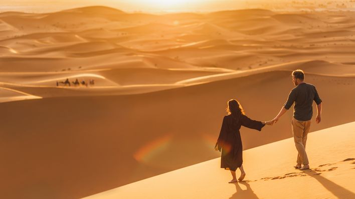 Paar geht über eine sandige Dünenlandschaft der Sahara, beleuchtet vom warmen Sonnenlicht