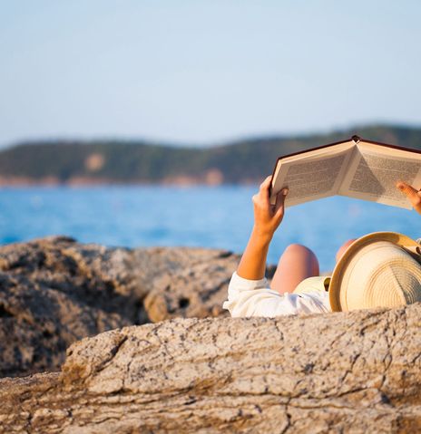 Frau auf Felsen am Meer mit Buch