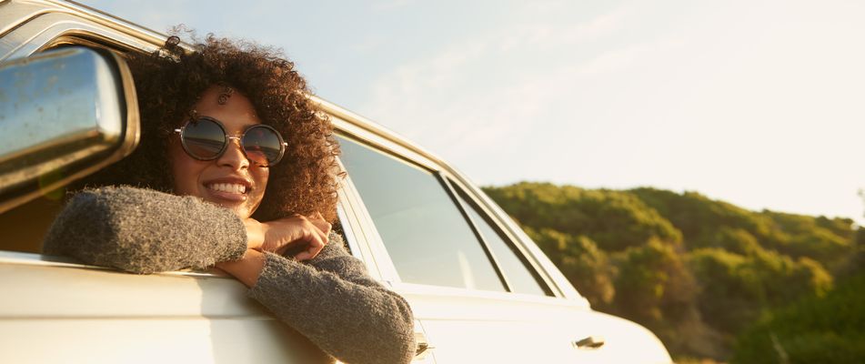 Frau mit Sonnenbrille schaut verträumt aus dem Autofenster in die Ferne