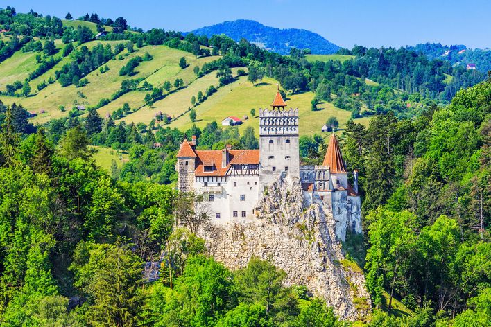 Schloss Bran erhebt sich über dichtem Wald und grünen Hügeln in der rumänischen Landschaft.