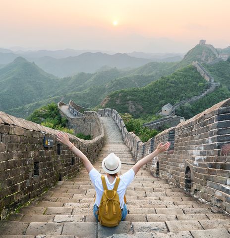 Frau sitzt mit ausgestreckten Armen auf der Großen Mauer in China und genießt den Ausblick