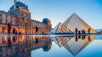 Louvre in Paris mit Glaspyramide und historischer Museumsfassade bei Sonnenuntergang