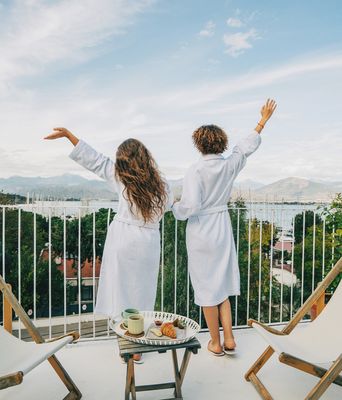 Zwei Frauen genießen den Ausblick von ihrem Hotel-Balkon auf einen Hafen
