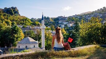 Frau sitzt vor den Toren der historischen Altstadt von Gjirokastra, eine weitere UNESCO-Weltkulturerbestätte mit charakteristischen Häusern und Festung