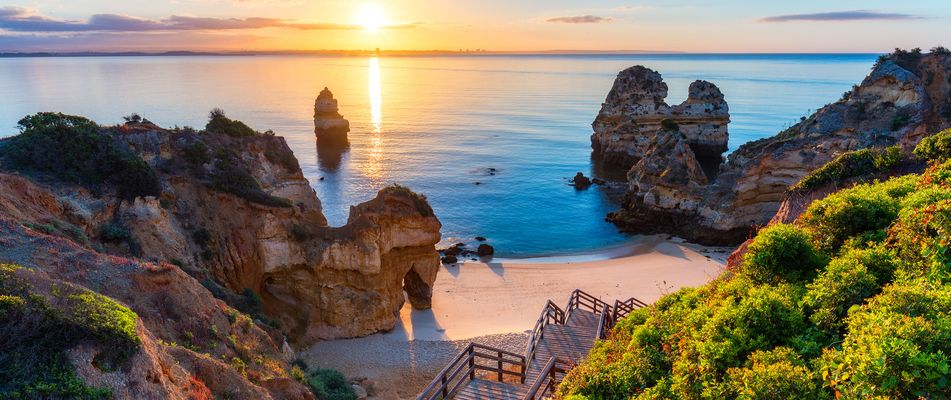 Die Sonne geht im warmen Abendlicht über einer kleinen Felsenbucht bei Lagos an der Algarve unter