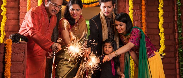 Indische Familie in traditioneller Kleidung feiert Diwali mit Wunderkerzen vor festlich geschmücktem Eingang