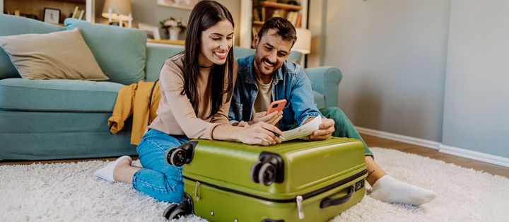 Familie packt lachend den Koffer für den Urlaub im Wohnzimmer