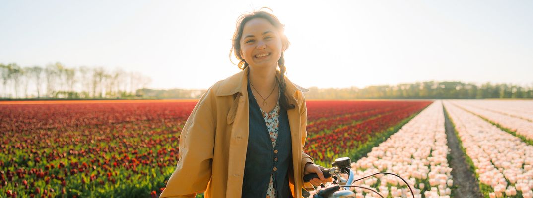 Frau steht mit einem Fahrrad vor einem bunten Tulpenfeld in Holland