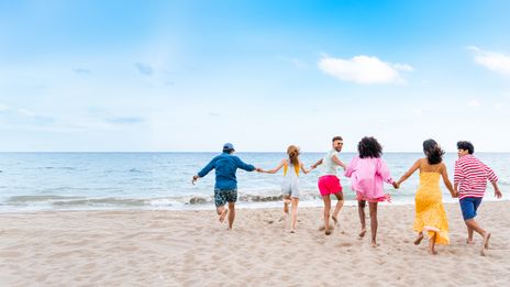 Gruppe junger Leute läuft Hand in Hand am Strand Richtung Meer