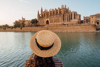 Frau mit Hut blickt auf die Kathedrale von Palma de Mallorca am Wasser bei Abendlicht
