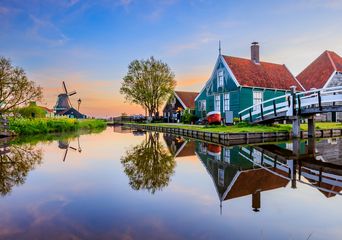 Idyllische Dorfkulisse mit Windmühle, Holzhäusern und spiegelndem Kanal in Zaanse Schans, Niederlande