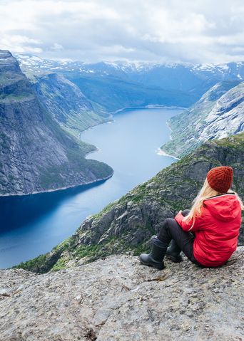 Eine Frau sitzt auf einem Felsen und schaut auf eine Fjordlandschaft