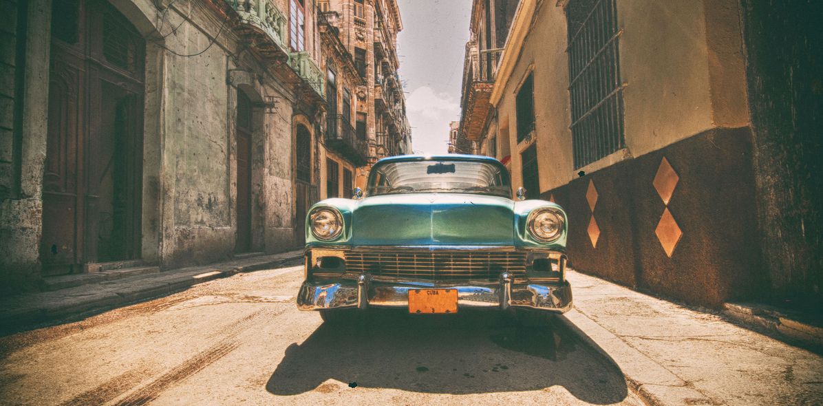 Typischer Oldtimer in Frontansicht in kubanischer Straße von alten Häusern umsäumt in Sepia-Farbe