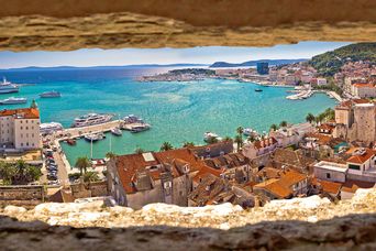 Panoramablick durch eine Felsnische über Häuser auf den Hafen von Split in Kroatien mit Booten und Schiffen auf dem Meer
