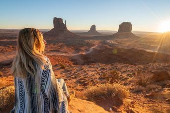 Frau in Rückansicht blickt über das Monument Valley in Arizona in den USA in den Sonnenuntergang