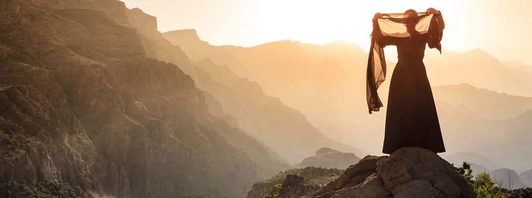 Frau steht auf Berg im Oman und blickt bei Sonnenuntergang über weite Landschaft