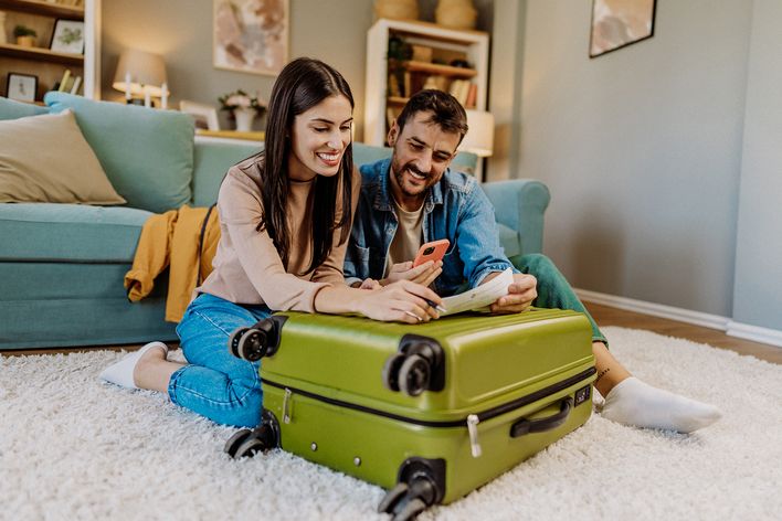Familie packt lachend den Koffer für den Urlaub im Wohnzimmer