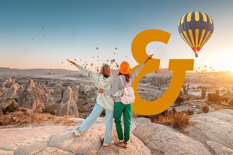 Paar jubelt bei Sonnenaufgang in Kappadokien mit Blick auf Heißluftballons und Tuffsteinfelsen